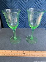 Pair of green glass wine glasses standing next to a wooden ruler showing height around 6 inches
