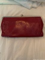 Red textured leather wallet/ clutch closed showing silver metal frame and kiss-lock closure.