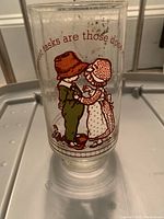 Glass featuring Holly Hobby and a boy character in vintage clothes with a printed phrase.
