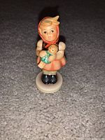 Front view of the Hummel figurine showing detailed painting and the girl in bonnet holding a doll.