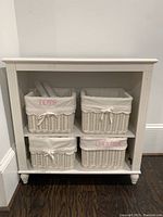 Full view of white shelf unit with four wicker baskets inside showing labels TOYS and GAMES.