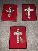 Three Lenox Christmas cross ornaments displayed in three red boxes with foam inserts, showing detailed designs and gold hanging tassels.