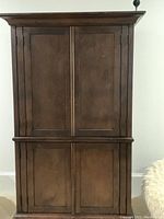 Front view of closed dark brown wooden four-door armoire with paneled doors and decorative crown molding on top