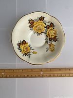 Top view showing small bone china bowl, white with yellow rose floral design and gold scalloped edge, ruler showing 5.5 inch diameter.