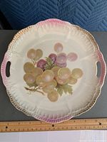 Front view of scalloped porcelain plate with painted grapes, fading pink and gold trim