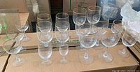 Set of 16 assorted stemmed crystal glasses with gold rims displayed on cardboard boxes. Includes wine glasses, water goblets, and smaller glasses. Glasses appear dusty and need cleaning.