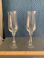 Two crystal toasting flutes standing upright showing full height and shape, etched pattern visible on bowls and faceted stems, placed on gray surface with blue quilted background.
