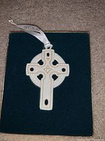 Celtic cross Christmas ornament shown on green felt inside box with white Wedgwood ribbon attached.