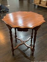 View of wood antique side table showing scalloped edge top with carved details and turned legs.
