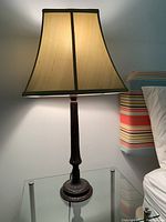 Full view of the lit table lamp showing dark brown wooden base and stem with light green fabric shade on glass-top table.