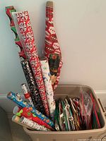 Photo showing multiple rolls of wrapping paper with red peppermint, black swirl, and holiday prints, and colorful birthday-themed rolls.