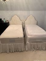 Two xtra long twin beds side by side with off white velvet scalloped headboards, mattresses, bed skirts.