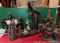 Full view of the nativity set displayed on red surface showing central figures including Baby Jesus, Mary, Joseph, palm trees, and Three Wise Men on horse, camel, and elephant.