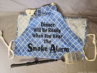 Blue BBQ apron with white grid and black text laid flat showing front design and straps.