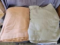 Two king size blankets folded, one beige and one light green, placed side by side on a chair or surface.