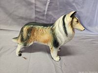 Side view of vintage ceramic Collie dog figurine on a light gray surface with cloth backdrop.