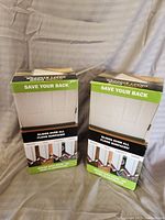 Photo of the two boxed door draft stoppers standing upright, showing front packaging and branding to save your back, glide on all floor surfaces.