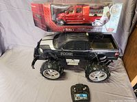 Two Ford truck models shown together: a large black Roose remote control monster truck and a boxed red Motor Max Ford F650 Super Crew model truck