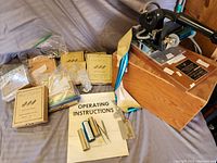 Franklin Matchbook Imprinter with original wooden storage box, operating instructions, foil rolls, and metal letters and numbers in boxes spread on a surface.