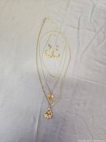 Full view of all three necklaces and pair of earrings laid out on a flat surface.