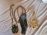 Photo showing three hand beaded medicine bags on fabric background: one leather with beadwork and fringe, two woven with bead and shell decorations.