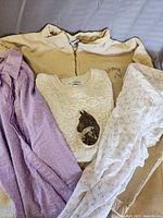 Photo of four horse-themed clothing items: cream zip pullover, white knit top with horse patch, purple cardigan, white knit top with ruffles and print.