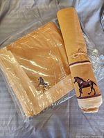 Light brown cotton tablecloth folded with visible horse design and matching rolled napkins tied with a string.