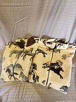 Two folded horse-themed fleece jackets stacked on a couch, one with brown collar patch visible, zipper front.