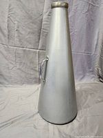 Photo of silver metal megaphone standing upright showing the tapered cone shape, metal handle, and metal rim at the narrow end.