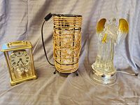 Three items together: brass clock, wicker lamp, and light-up glass angel figurine.