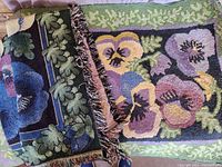 Photo showing folded pansy floral rug and partial view of matching throw with colorful floral pansy pattern and fringe.
