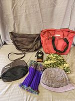 General view of five main items in the lot: brown leather purse, pink/red tote bag, black mesh pouch, two knit hats, and purple gloves.