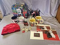 Overview photo showing four mugs, red cap with Scottie designs, wooden Scottie dog toy on wheels, cards and charms, and holiday tin with Westie design