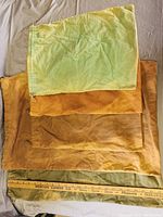 Top-down view of 5 faded cloth storage bags in different sizes and colors stacked overlapping, ruler at bottom for size reference