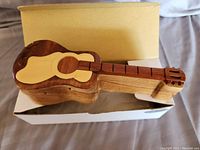 Photo of the wood guitar puzzle box showing the assembled guitar shape with light and dark wood tones and guitar string inlays on the neck.