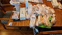 Photo showing multiple pairs of ballet pointe shoes with satin finish along with elastic bands and accessories on wooden table.