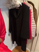 Assorted women's coats including black, bright pink, beige puffer, and brown fur-like coat hung in closet