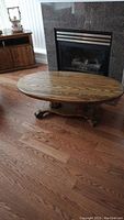 Photo of the wooden oval coffee table placed in front of a fireplace on hardwood floor, showing top view and surface condition