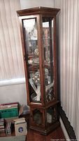Front view of the tall brown wood and glass display cabinet showing interior shelves and lighting fixture at the top.
