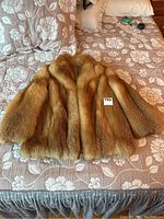 Front view of fox fur coat laid flat on patterned bedspread with lot sticker visible