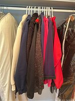 Photo showing nine assorted women's hoodies and jackets hung on a rack in various colors including beige, navy, brown, purple, pink, red, and black plastic covering one jacket.