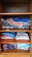 Folded nightdresses and pajama bottoms in assorted floral and solid colors displayed on wooden shelving