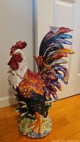 Front side view of the colorful metal rooster statue showing detailed feathers and vibrant paint.