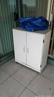 Front view of white storage cupboard with blue tarp on top, placed on tiled floor near sliding glass door.