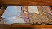 Drawer with white lace and embroidery tablecloths, napkins, and some pink cloths