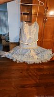 Full view of light blue ballet tutu dress with cream lace floral appliqués on bodice and skirt, hanging on hanger