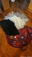 Two practice tutus (black and white) laid on a floor alongside a red floral tutu bag with handles.