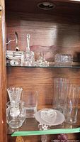 Shelf showing an assortment of vintage crystal and glass items including vases, bell, trinket boxes, and pedestal bowl