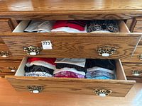 Two open drawers of a wooden dresser showing neatly folded women's tops of various colors and patterns.