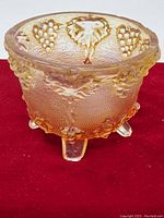 Side view of the amber Depression glass footed bowl with detailed grape and leaf pattern and three feet